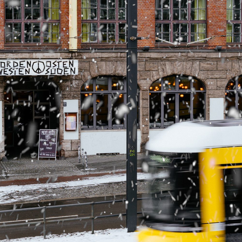 Snow is falling around the Michelberger Hotel in Berlin and a tram is passing by.